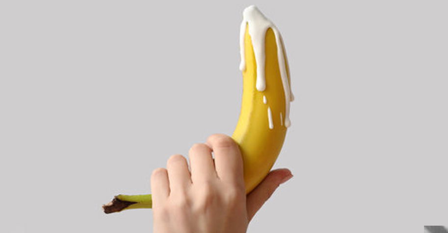 hand holding a ripe banana coated with dripping white liquid